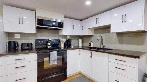 a kitchen with white cabinets and black appliances at Cozy Basement Apartment for 4 - Near Cafes & Parks in Toronto