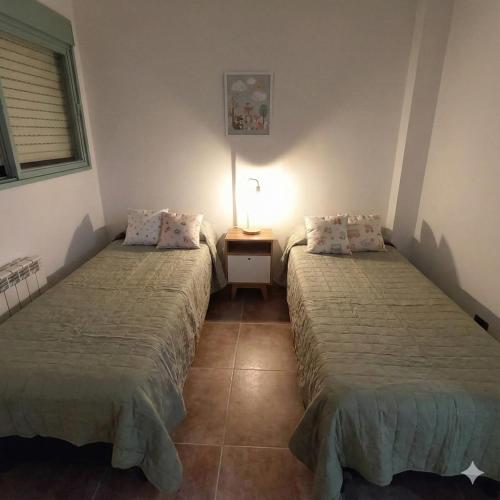 a room with two beds and a table with a lamp at Trelew Cartref-Departamento Familiar Cerca del centro in Trelew