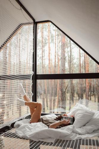 a woman laying in bed reading a book in front of a window at Wyjątkowy domek w kompleksie Patyki Las Możliwości in Zelów