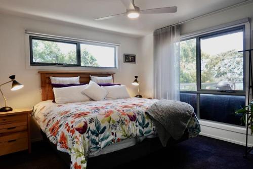 a bedroom with a bed with a floral bedspread and two windows at Paradise - Spacious, Ocean Views, Outdoor Living in Dodges Ferry