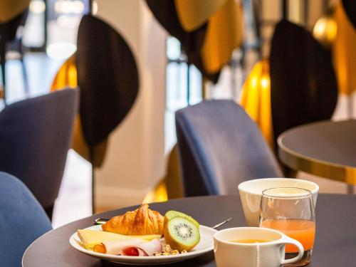 una mesa con un plato de comida y una taza de zumo de naranja en Mercure Toulouse Aeroport Blagnac, en Blagnac