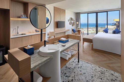 a hotel room with a bed and a sink and a mirror at Hoi An Royal Beachfront Resort & Villas in Dien Ban