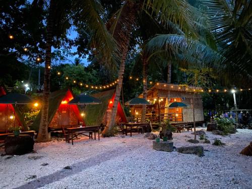 Alfonsa Tent Ground - Camp By The Sea في أوسلوب: منتجع به طاولات ومظلات على الشاطئ ليلاً