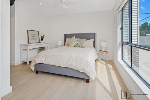 a white bedroom with a bed and a window at Bay Dream. in Malua Bay