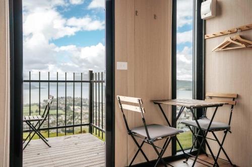 Black Horse Cabin 3 by Tiny Away في Waitoki: بلكونه فيها كرسيين وطاولة مطلة