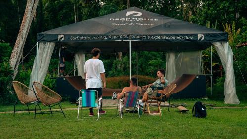 a group of people sitting in chairs under an umbrella at Drop House Hostel - Surf & Skate - Itamambuca in Ubatuba