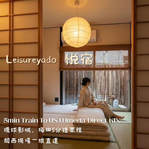 a woman sitting on a bed looking out the window at Leisureyado USJ 5 min train 悦宿西九条 in Osaka