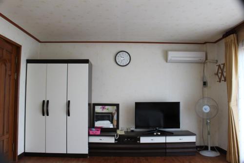 a living room with a tv and a clock on the wall at Jeju Feel House in Jeju