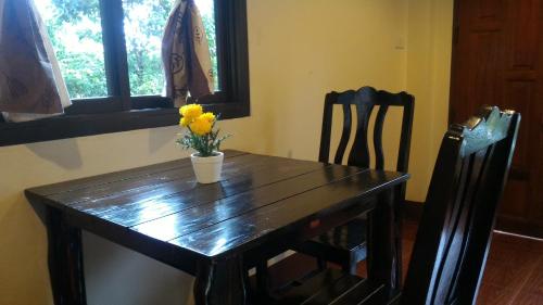 a wooden table with a vase of yellow flowers on it at Baan-kawkaew-kata in Ban Karon