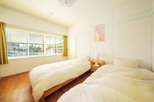 twee bedden in een witte kamer met een raam bij Matsumoto Inn in Matsumoto