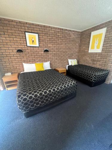 a bedroom with two beds and a brick wall at Cessnock Vintage motor inn in Cessnock