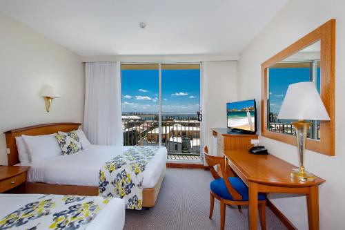 ニューカッスルにあるNoah's On the Beachのベッド2台、デスク、窓が備わるホテルルームです。
