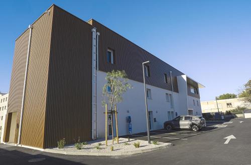 a large building with a car parked in a parking lot at Kyriad Montpellier Sud - Lattes in Montpellier