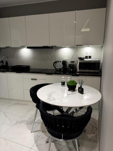 a kitchen with a white table and black chairs at Apartamenty Prestiż Podfigórna 200 metrów od centrum in Koszalin
