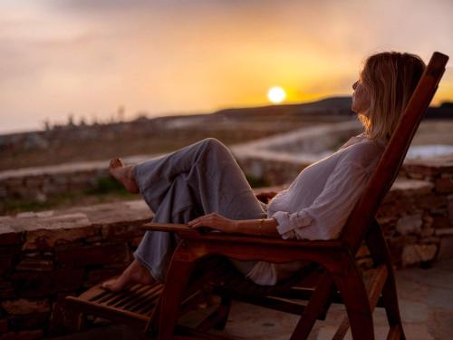 a woman sitting in a chair watching the sunset at Moniasma Rustic Stone House in Folegandros in Ano Meria