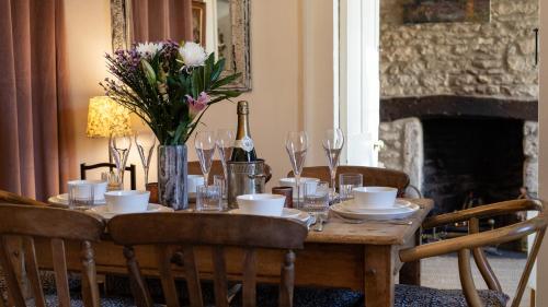 a wooden table with a vase of flowers and wine glasses at Bell Cottage in Charlbury
