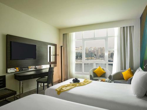 Novotel Cairo El Borg في القاهرة: غرفة فندقية تحتوي على سريرين ومكتب ونافذة