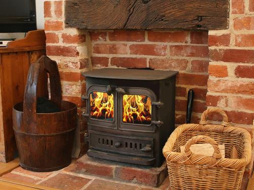 een houtkachel in een bakstenen open haard met een mand bij Valley Farm Cottage in Sudbourne