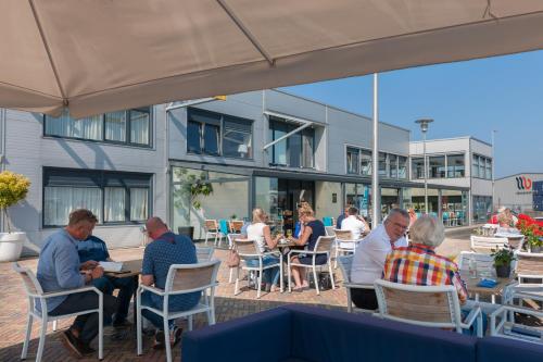 a group of people sitting at tables outside a building at Hotel de Boegschroef in Delfzijl
