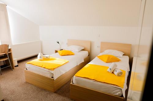 two beds in a hotel room with yellow sheets at London Rooms Zagreb Airport in Velika Gorica
