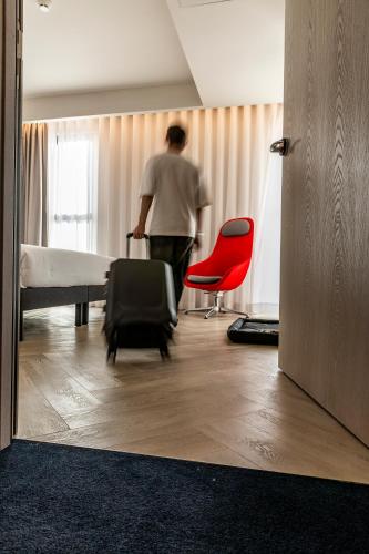 a man walking through a room with a bed and a red chair at Holiday Inn Express Porto - Boavista by IHG in Porto
