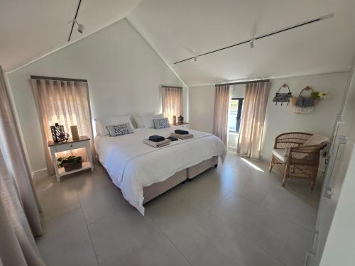 a white bedroom with a bed and a chair at Yzer Heights Relaxed Luxury Stay in Yzerfontein