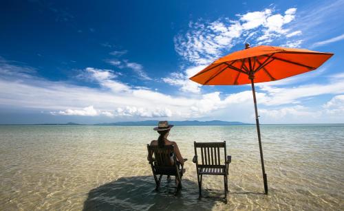 a woman sitting in a chair under an umbrella on the beach at Chantaramas Beach Resort Koh Phangan in Baan Khai
