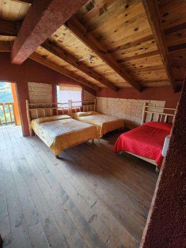 two beds in a large room with wooden ceilings at Cabañas La Moneda in Rancho La Carolina