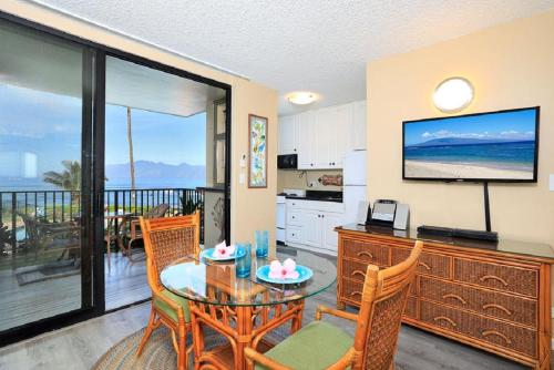 a living room with a table and a kitchen with a television at Noelani 113 in Kahana