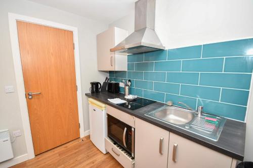 eine Küche mit einer Spüle und einer blauen Kachelwand in der Unterkunft Convenient Budget Studio in Central Sheffield in Midland