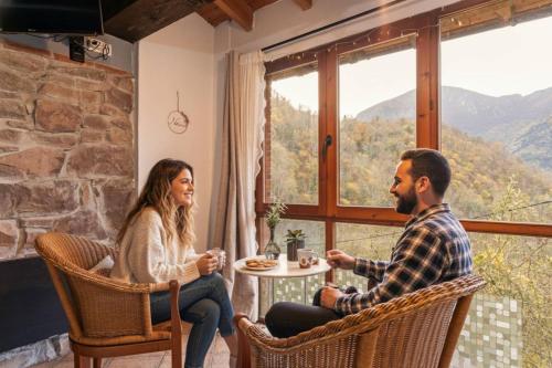 a man and woman sitting at a table in a room with a window at Carbayu Senda del Oso in Proaza