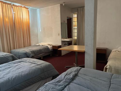 a room with three beds and a wooden table at Hotel Los Proceres in La Aurora