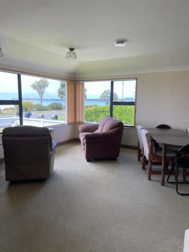 a living room with two chairs and a table and windows at Tranquil Tides in Motueka