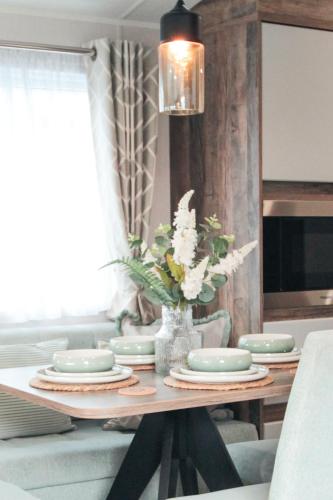 a dining room table with plates and a vase of flowers at Harbour View at Avocet Crescent - Luxury Lodge with Hot Tub - Hayling Island - Mill Rythe Holiday Village in North Hayling