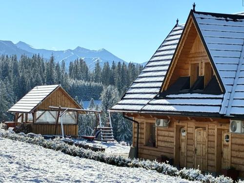 two wooden buildings in the snow with mountains in the background at Witowiańskie Domki z prywatnym jacuzzi i kominkiem in Dzianisz