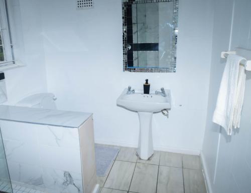 Un baño blanco con lavabo y espejo. en HAPPY HOME Guest house, en Gqeberha