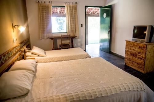a bedroom with two beds and a television and a door at Pousada e Espaço Flor da Serra in Cruzeiro