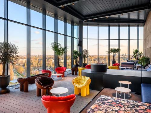 un vestíbulo con sillas coloridas, mesas y ventanas en TRIBE Budapest Stadium, en Budapest