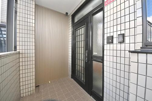 a hallway with black doors and white tiled walls at LIJ Stay Morinomiya 5BedRooms in Osaka