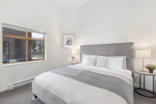 a white bedroom with a large bed and a window at Olympic Plaza Views with Pool and Hot Tub by Harmony Whistler in Whistler