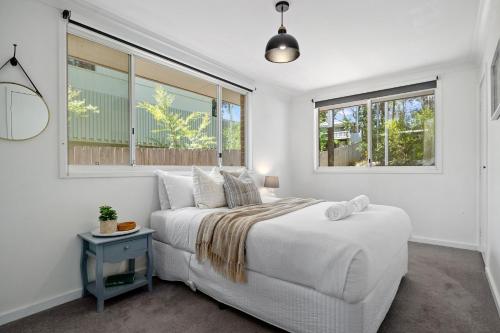 a bedroom with a white bed and two windows at Bluegum Beach Stay in Narrawallee