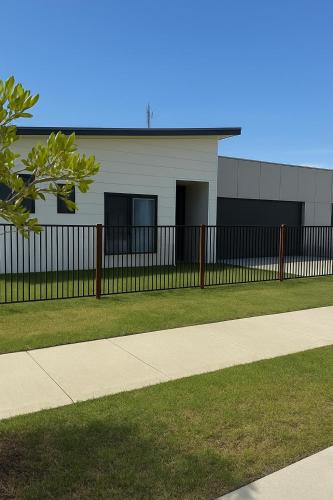 a fence in front of a building with a sidewalk at Azure Abode in Broulee