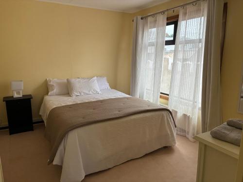 Un dormitorio con una cama y una ventana grande. en Hostal Mundet, en Punta Arenas