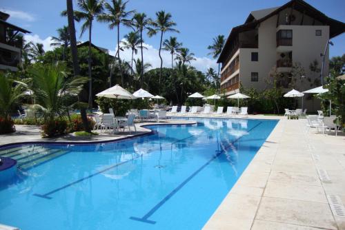 a swimming pool with chairs and umbrellas at a resort at Nannai Beira Mar Porto de Galinhas 307 in Porto De Galinhas