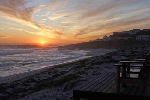 a sunset at the beach with a bench on the beach at On The Beach Apartments in Yzerfontein