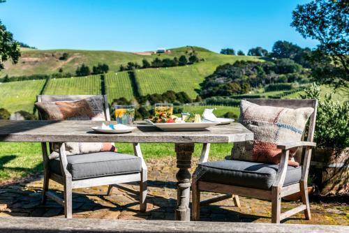 The Vineyard Cottage - Stay Waiheke في Onetangi: طاولة مع صحن من الطعام و كرسيين
