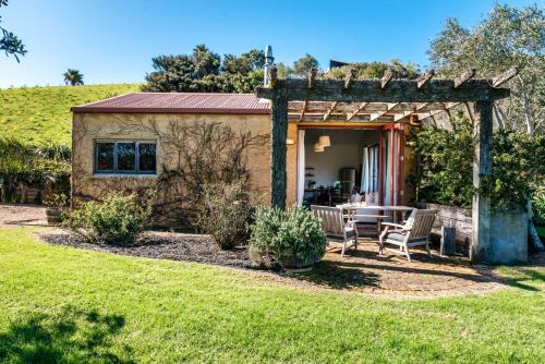 The Vineyard Cottage - Stay Waiheke في Onetangi: منزل به طاولة وكراسي في ساحة