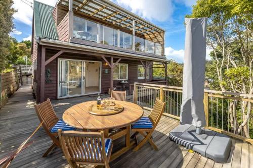 a house with a wooden deck with a wooden table and chairs at Seahorse Cottage - Stay Waiheke in Waiheke Island