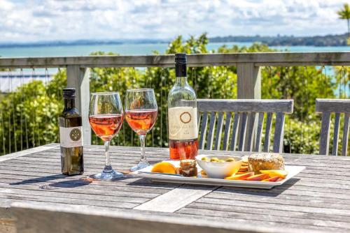 a table with two glasses of wine and a plate of food at Black Cottage - Stay Waiheke in Waiheke Island