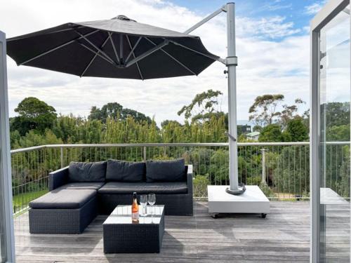 un patio con sofá negro y sombrilla en Beachlovers Onetangi - Stay Waiheke, en Waiheke Island
